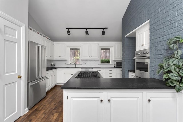 kitchen with appliances with stainless steel finishes, dark hardwood / wood-style flooring, tasteful backsplash, white cabinetry, and lofted ceiling