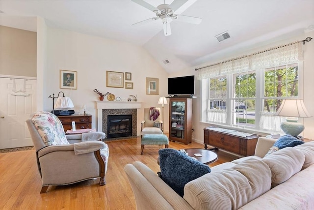 living area featuring a glass covered fireplace, lofted ceiling, a ceiling fan, and wood finished floors