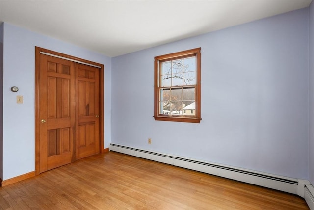 unfurnished bedroom featuring baseboards, a closet, a baseboard heating unit, and wood finished floors