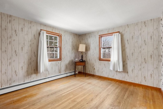 unfurnished room with wallpapered walls, a baseboard radiator, hardwood / wood-style flooring, and baseboards