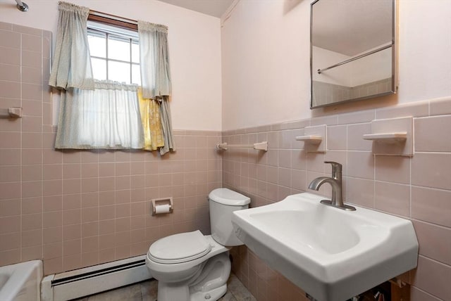 bathroom with toilet, a baseboard heating unit, a wainscoted wall, a sink, and tile walls