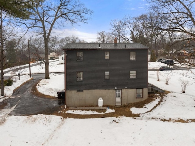 snow covered rear of property with a chimney