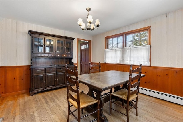 dining area with light wood-type flooring, wainscoting, baseboard heating, and an inviting chandelier