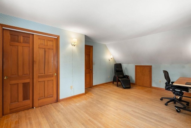 office area with light wood-style floors, vaulted ceiling, baseboards, and wallpapered walls