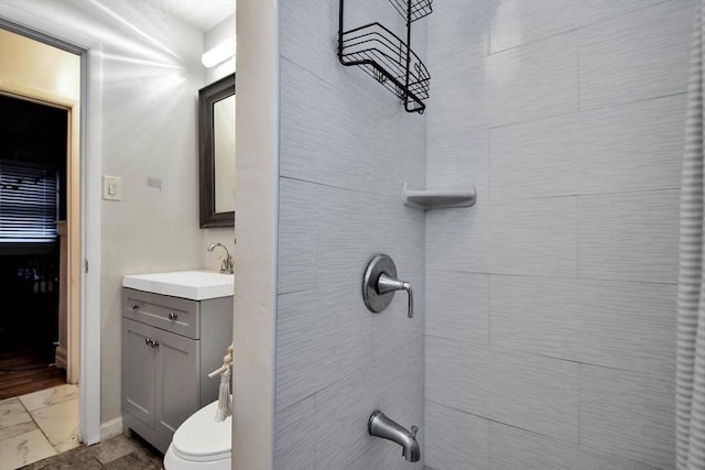 bathroom with marble finish flooring, vanity, tiled shower, and toilet