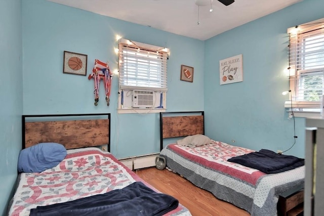 bedroom with baseboard heating, cooling unit, wood finished floors, and ceiling fan
