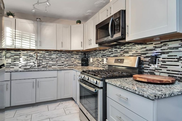 kitchen with appliances with stainless steel finishes, light marble finish floors, a sink, light stone counters, and tasteful backsplash