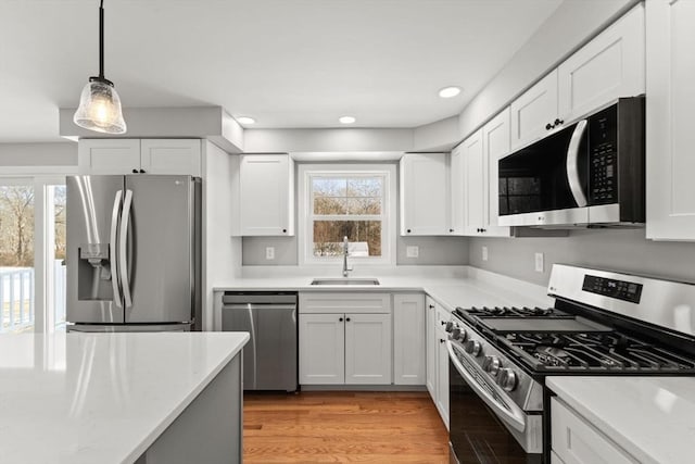 kitchen featuring sink, stainless steel appliances, light hardwood / wood-style floors, white cabinets, and decorative light fixtures