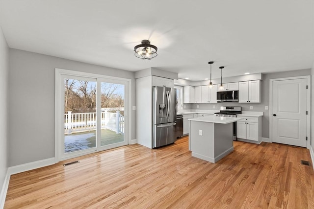 kitchen featuring white cabinetry, stainless steel appliances, a kitchen island, decorative light fixtures, and light wood-type flooring