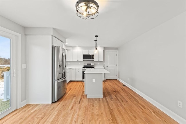 kitchen featuring a kitchen island, appliances with stainless steel finishes, decorative light fixtures, white cabinetry, and light wood-type flooring