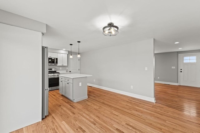 kitchen featuring a kitchen island, appliances with stainless steel finishes, pendant lighting, and light hardwood / wood-style floors