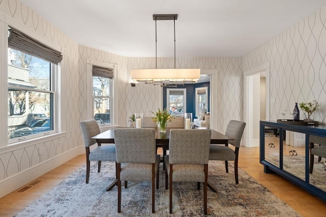 dining space with wallpapered walls, baseboards, visible vents, and wood finished floors