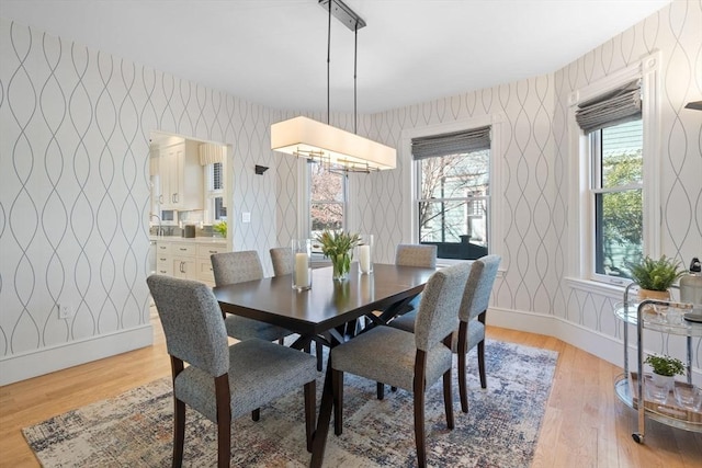 dining room with light wood finished floors, baseboards, and wallpapered walls