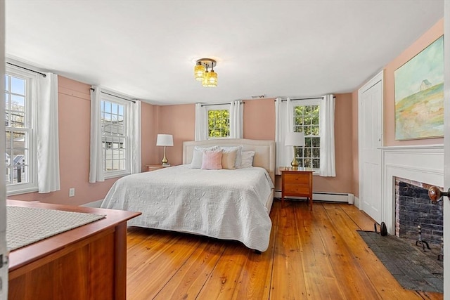 228 Main St, Groton, MA 01450 - bedroom featuring a fireplace with flush hearth, baseboard heating, and light wood-style floors