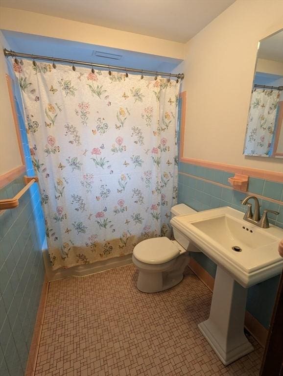 bathroom with toilet, shower / bath combo, wainscoting, tile patterned floors, and tile walls
