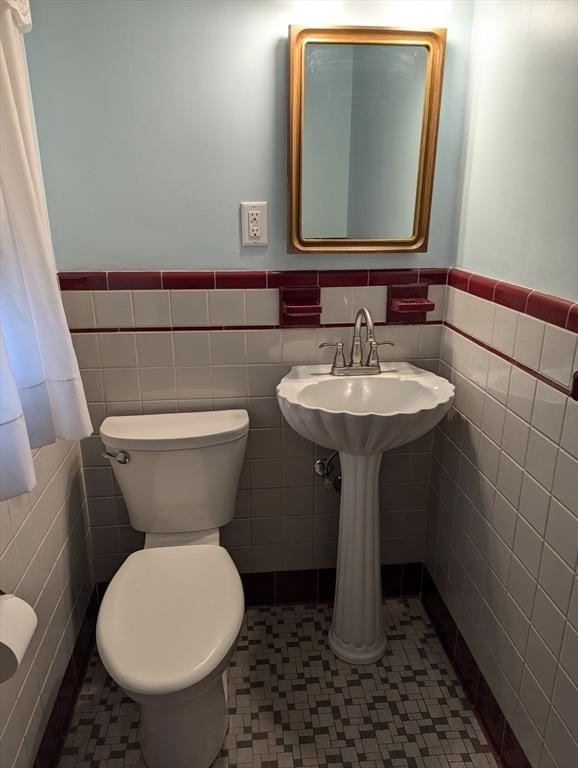 bathroom featuring tile walls, toilet, and wainscoting