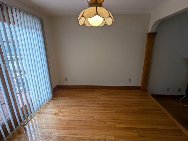 spare room featuring arched walkways, light wood finished floors, and baseboards