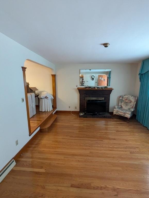 living room with a baseboard heating unit, baseboards, light wood-style flooring, and a fireplace