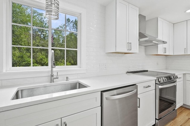 kitchen with wall chimney range hood, appliances with stainless steel finishes, light countertops, and a sink