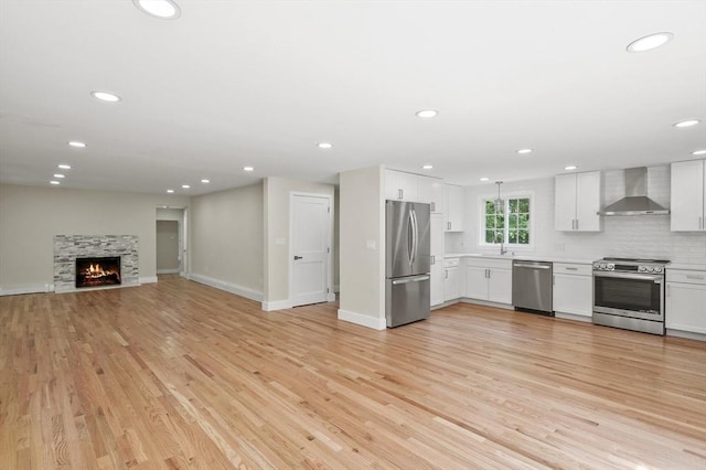 kitchen with wall chimney exhaust hood, appliances with stainless steel finishes, light wood-type flooring, and white cabinets