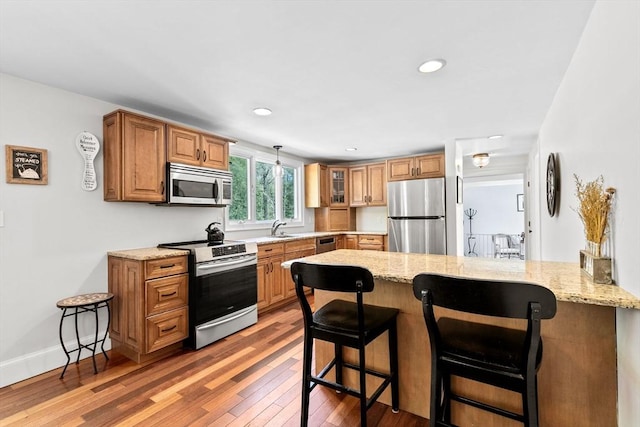 59 First Parish Rd, Norwell, MA 02061 - kitchen featuring stainless steel appliances, a kitchen bar, a peninsula, light stone counters, and light wood-style flooring