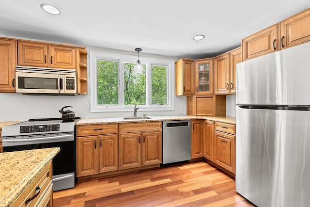 59 First Parish Rd, Norwell, MA 02061 - kitchen featuring appliances with stainless steel finishes, light wood finished floors, light stone countertops, brown cabinetry, and pendant lighting