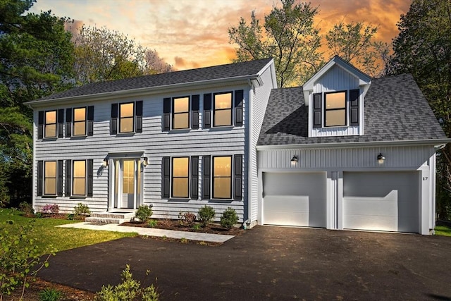colonial-style house with asphalt driveway, a garage, and roof with shingles