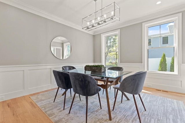 dining area featuring ornamental molding, light wood finished floors, healthy amount of natural light, a decorative wall, and wainscoting