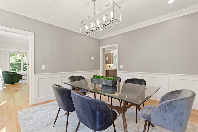 dining space with ornamental molding, light wood finished floors, a wainscoted wall, a chandelier, and a decorative wall