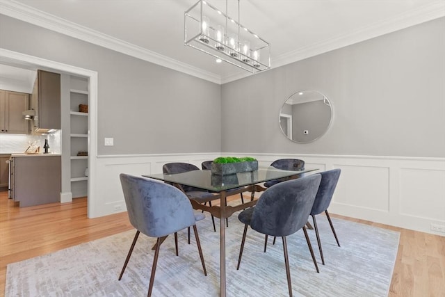 dining space with light wood-style flooring, crown molding, a decorative wall, a chandelier, and wainscoting
