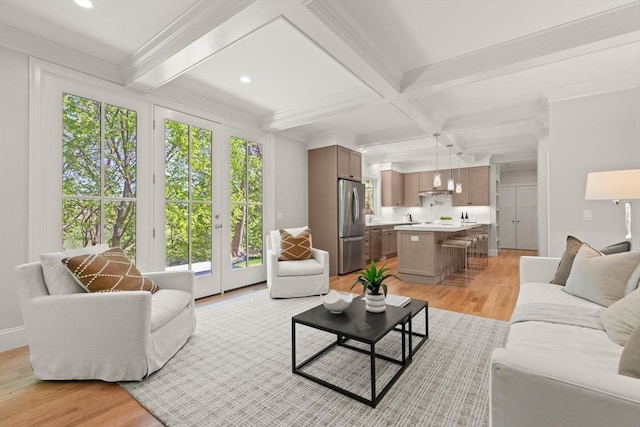 living room featuring plenty of natural light, light wood-style floors, beam ceiling, coffered ceiling, and ornamental molding