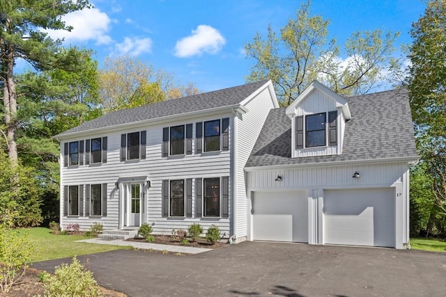 colonial inspired home with asphalt driveway, an attached garage, and roof with shingles