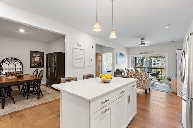 kitchen with light stone counters, light wood-style floors, freestanding refrigerator, white cabinetry, and a kitchen island