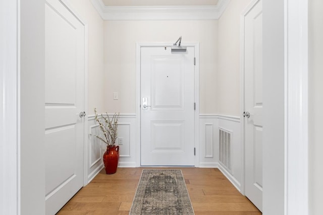 doorway with crown molding, wainscoting, and a decorative wall