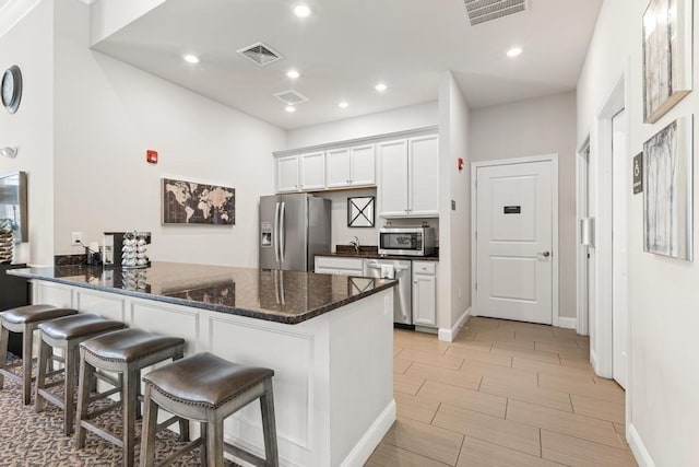 kitchen with dark stone counters, appliances with stainless steel finishes, visible vents, and a kitchen bar