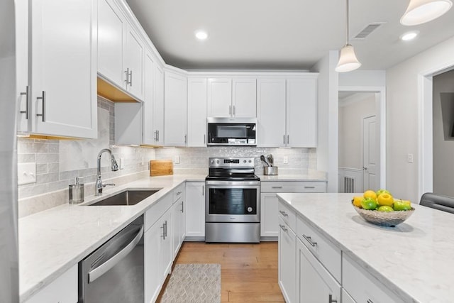 kitchen with a sink, white cabinets, pendant lighting, and stainless steel appliances