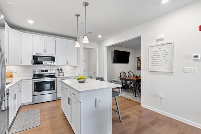 kitchen with a kitchen breakfast bar, a center island, tasteful backsplash, stainless steel appliances, and white cabinetry