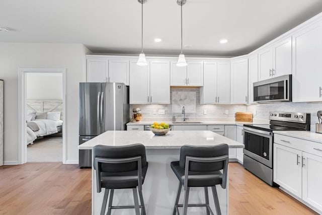 kitchen featuring a kitchen island, a sink, light wood finished floors, a breakfast bar, and stainless steel appliances