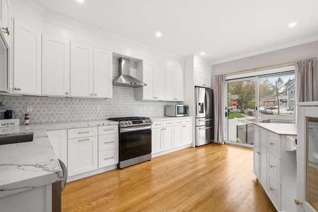 kitchen with wall chimney exhaust hood, appliances with stainless steel finishes, light wood finished floors, white cabinets, and backsplash
