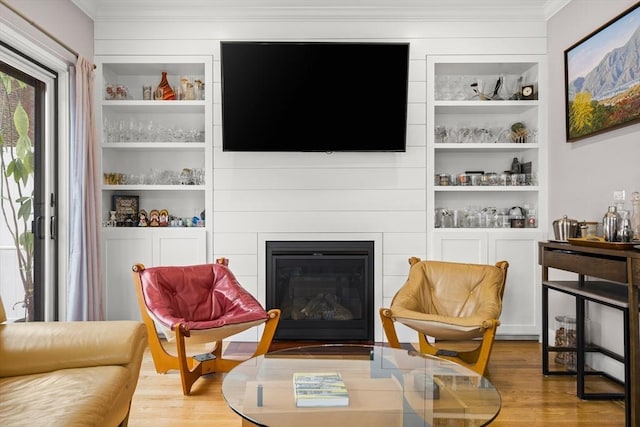 sitting room featuring crown molding, wood finished floors, built in shelves, and a fireplace