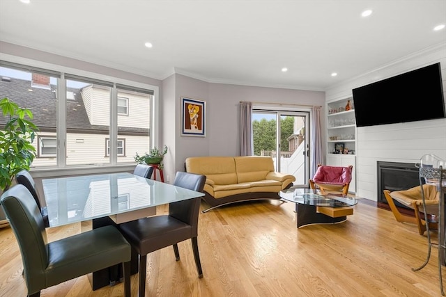 living area featuring crown molding, built in shelves, light wood-style floors, a glass covered fireplace, and recessed lighting
