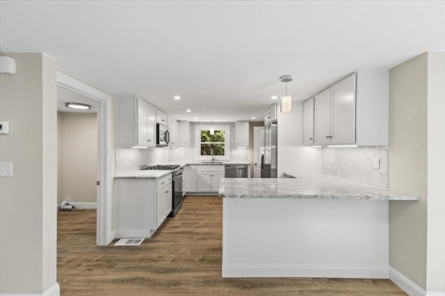 kitchen with white cabinets, decorative light fixtures, stainless steel appliances, kitchen peninsula, and light stone counters