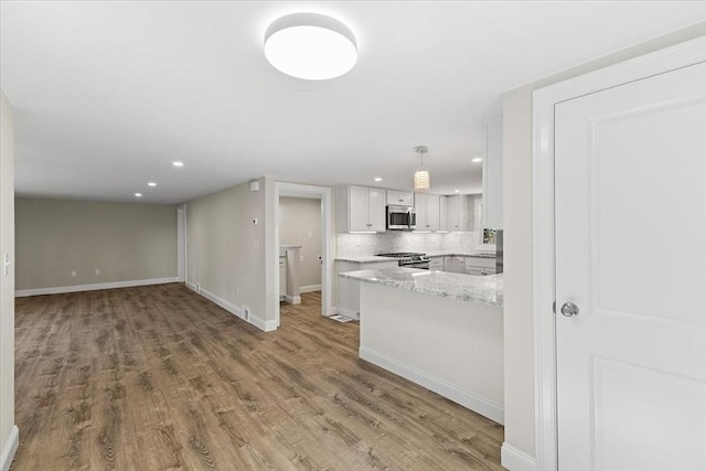 kitchen with white cabinetry, kitchen peninsula, appliances with stainless steel finishes, decorative light fixtures, and wood-type flooring