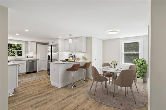 kitchen with light hardwood / wood-style floors, kitchen peninsula, decorative backsplash, appliances with stainless steel finishes, and white cabinets