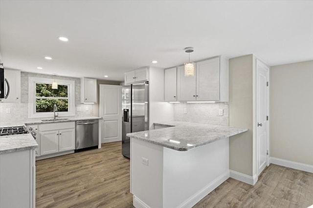 kitchen with kitchen peninsula, stainless steel appliances, pendant lighting, white cabinets, and sink