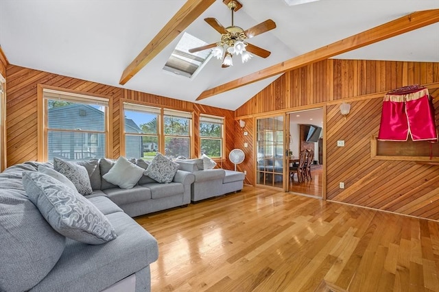 living room with wooden walls, light wood-style flooring, ceiling fan, and a skylight