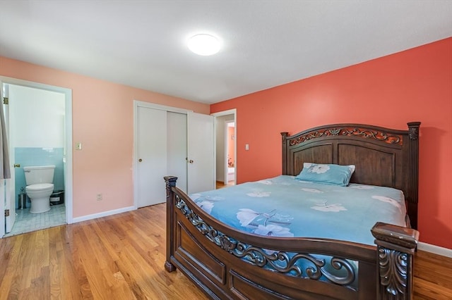 bedroom featuring light wood-style flooring, baseboards, ensuite bath, and a closet