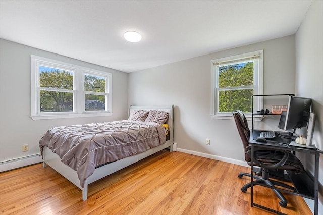 bedroom with light wood-style flooring, an office area, baseboard heating, and baseboards