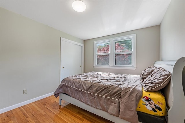 bedroom with light wood-type flooring, a closet, and baseboards