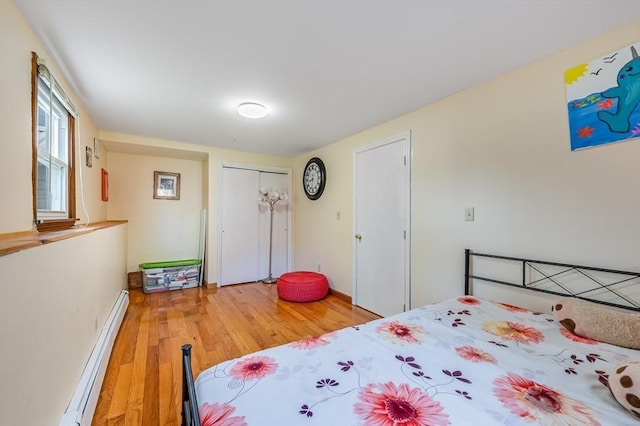 bedroom featuring a baseboard radiator, light wood finished floors, a closet, and baseboards
